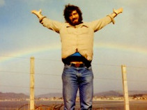 Young Glen standing with his arms held high with a rainbow arching across the sky behind him